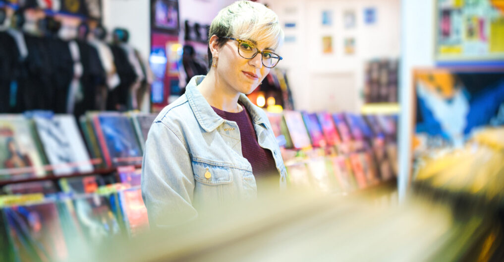 Young Woman Browsing Through Vintage Discs and Choosing Vinyl LP In Records Shop. Portrait of Customer Smiling At Camera And Buying Music Albums.