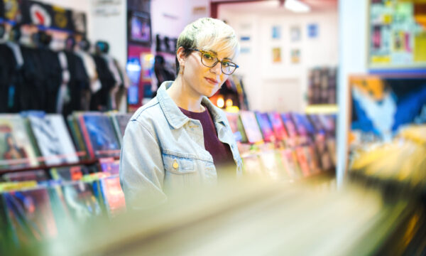Young Woman Choosing Vintage Vinyl LP In Records Shop Young Woman Browsing Through Vintage Discs and Choosing Vinyl LP In Records Shop. Portrait of Customer Smiling At Camera And Buying Music Albums.