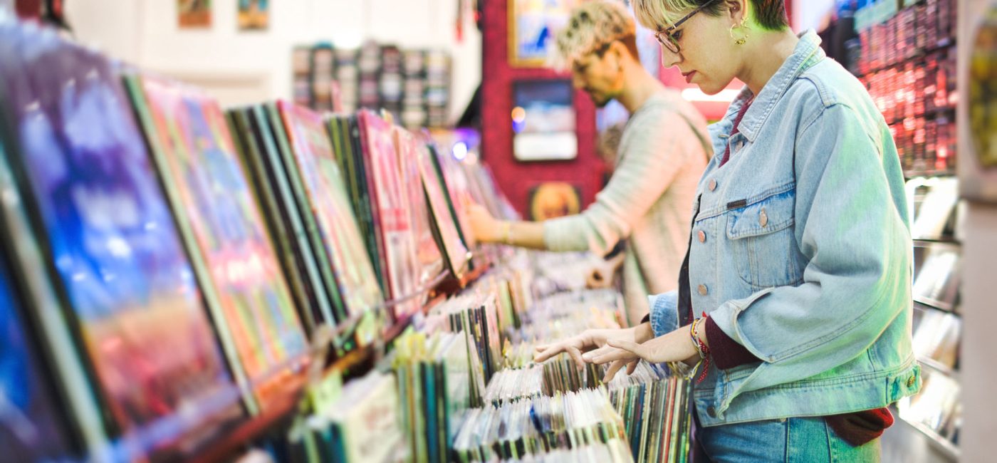 Young Woman And Man Browsing Through Vintage Discs and Choosing Vinyl LP In Records Shop. Couple Buying Music Albums.